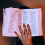 A close-up of a hand holding an open Bible, displaying Proverbs under warm lighting.